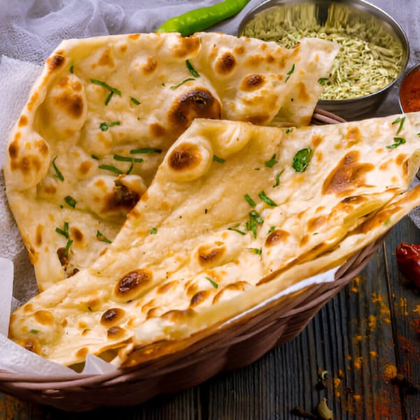 Freshly baked Indian naan bread with herbs in a basket, alongside green chilies and spices.
