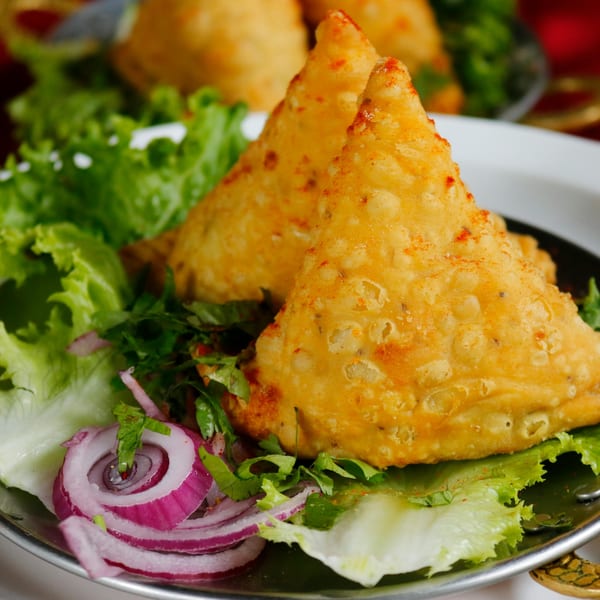 Two golden-brown samosas, sprinkled with spices, served on a bed of fresh lettuce and red onion.