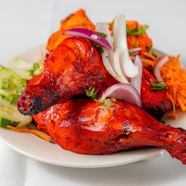 Two vibrant red Tandoori chicken drumsticks garnished with sliced onions, carrots, and cucumber on a white plate.
